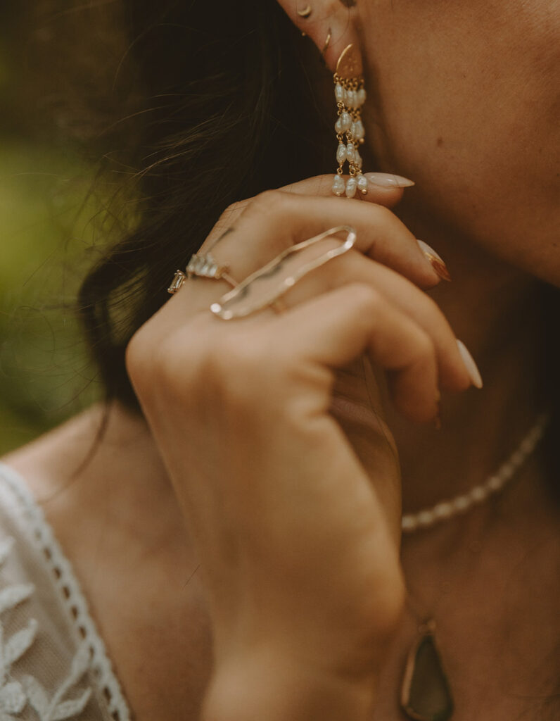 Close-up of the bride wearing dangling pearl earrings, pearl necklace, and a ring