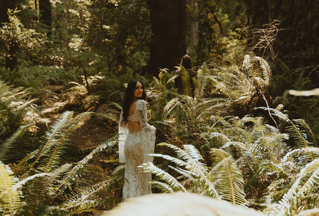 bride in a white lace dress standing amongst lush, green ferns in a forest