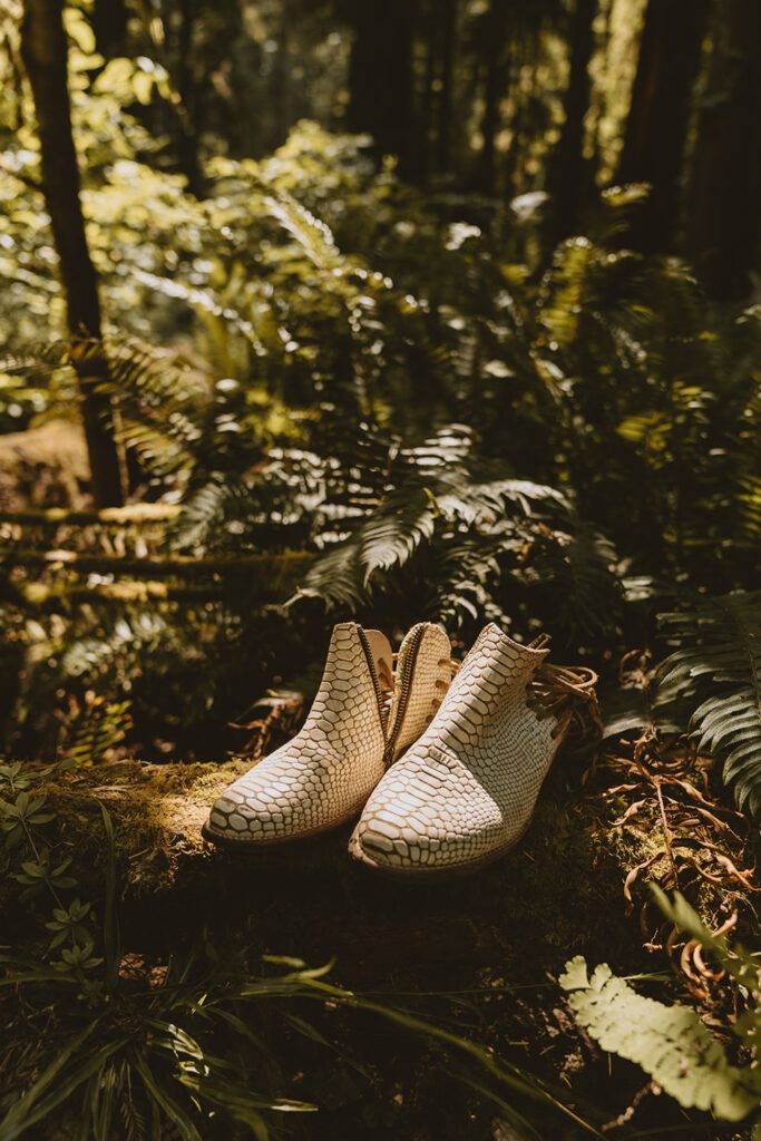 pair of white, snake-patterned ankle boots placed on a mossy log