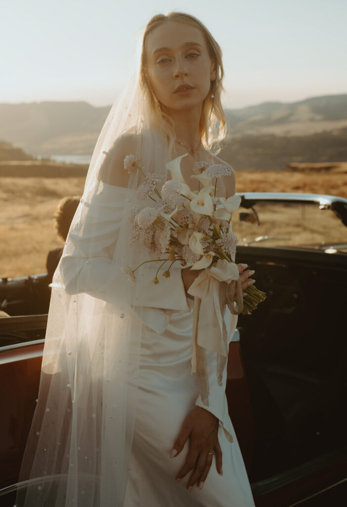 bride standing next to a car holding her wedding bouquet