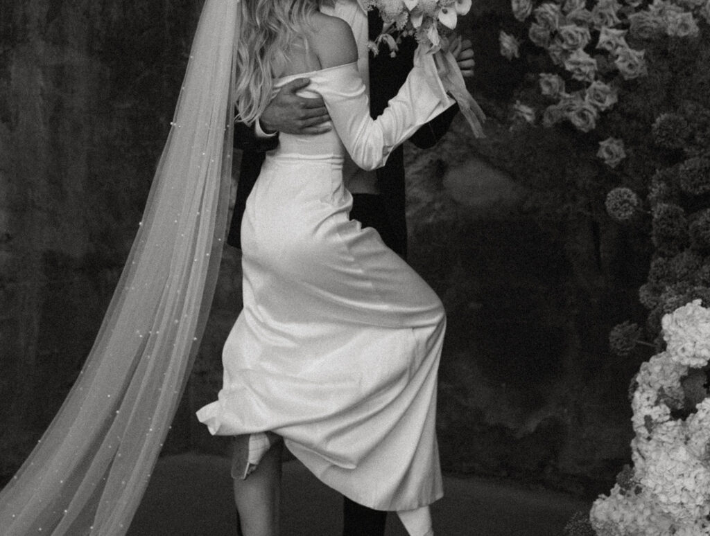 A black-and-white photo shows a bride and groom embracing each other