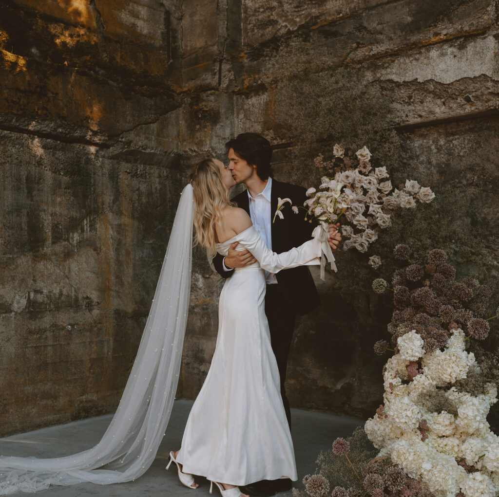 bride and groom kissing in a rustic setting with earthy, weathered walls
