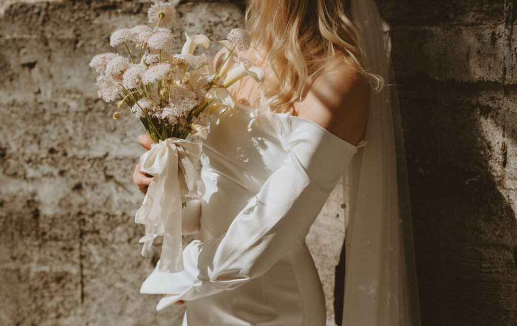 bride in a white off-the-shoulder bridal gown holds a bouquet