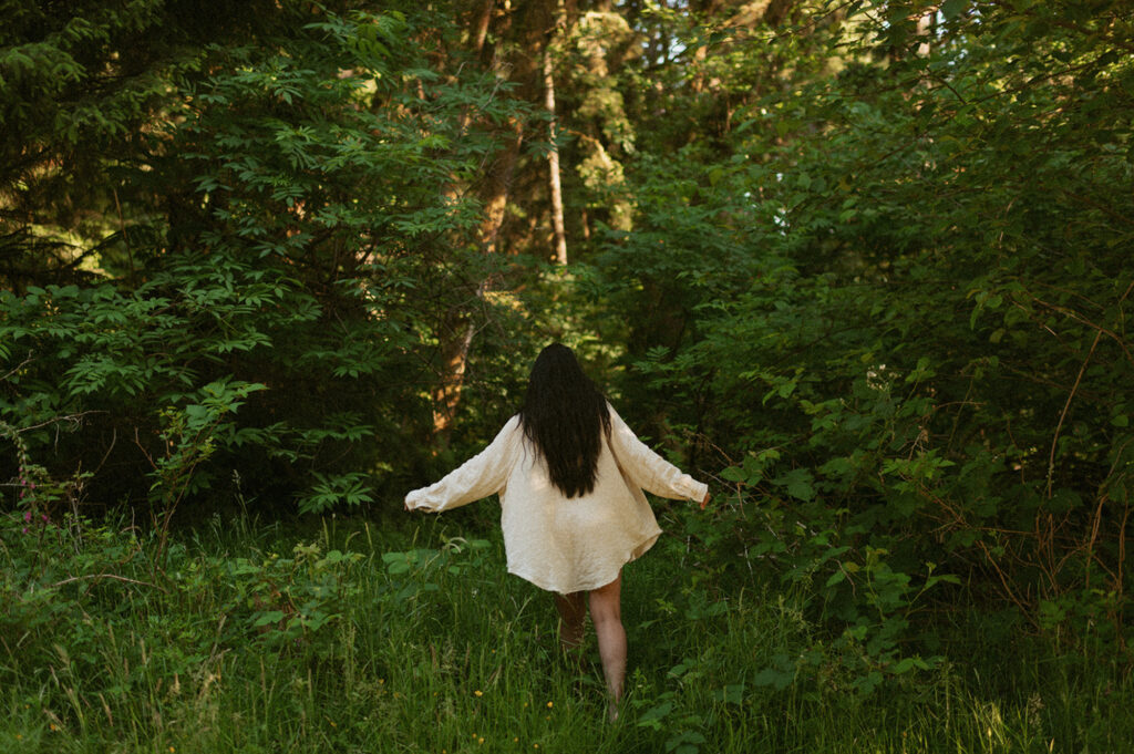 Person wearing a light-colored, long-sleeved shirt walks through a lush, green forest