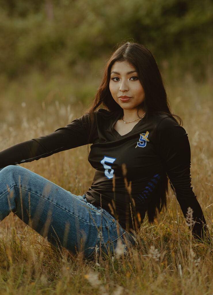 A woman sitting in a grassy field wearing a black long-sleeve shirt and blue jeans