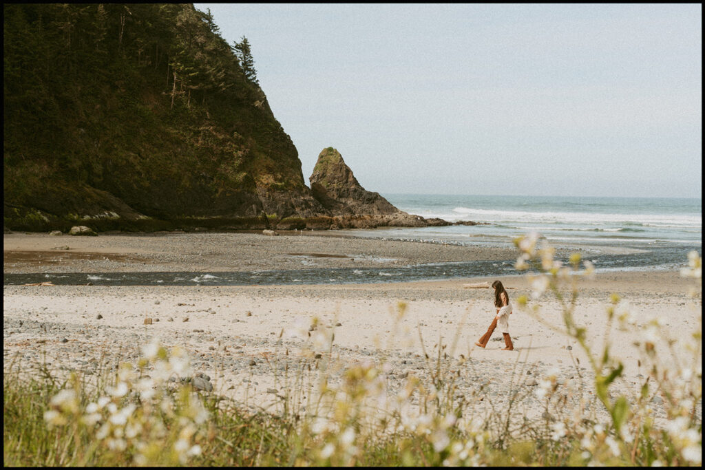 Woman walking along a sandy beach with gentle waves in the background in Florence, Oregon for her senior beach photo shoot