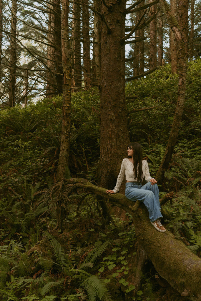 Woman with long hair sitting on a moss-covered tree branch in a forest