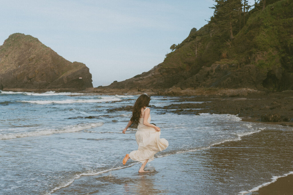 Woman in a white dress runs playfully through shallow surf on a beach in Florence, Oregon