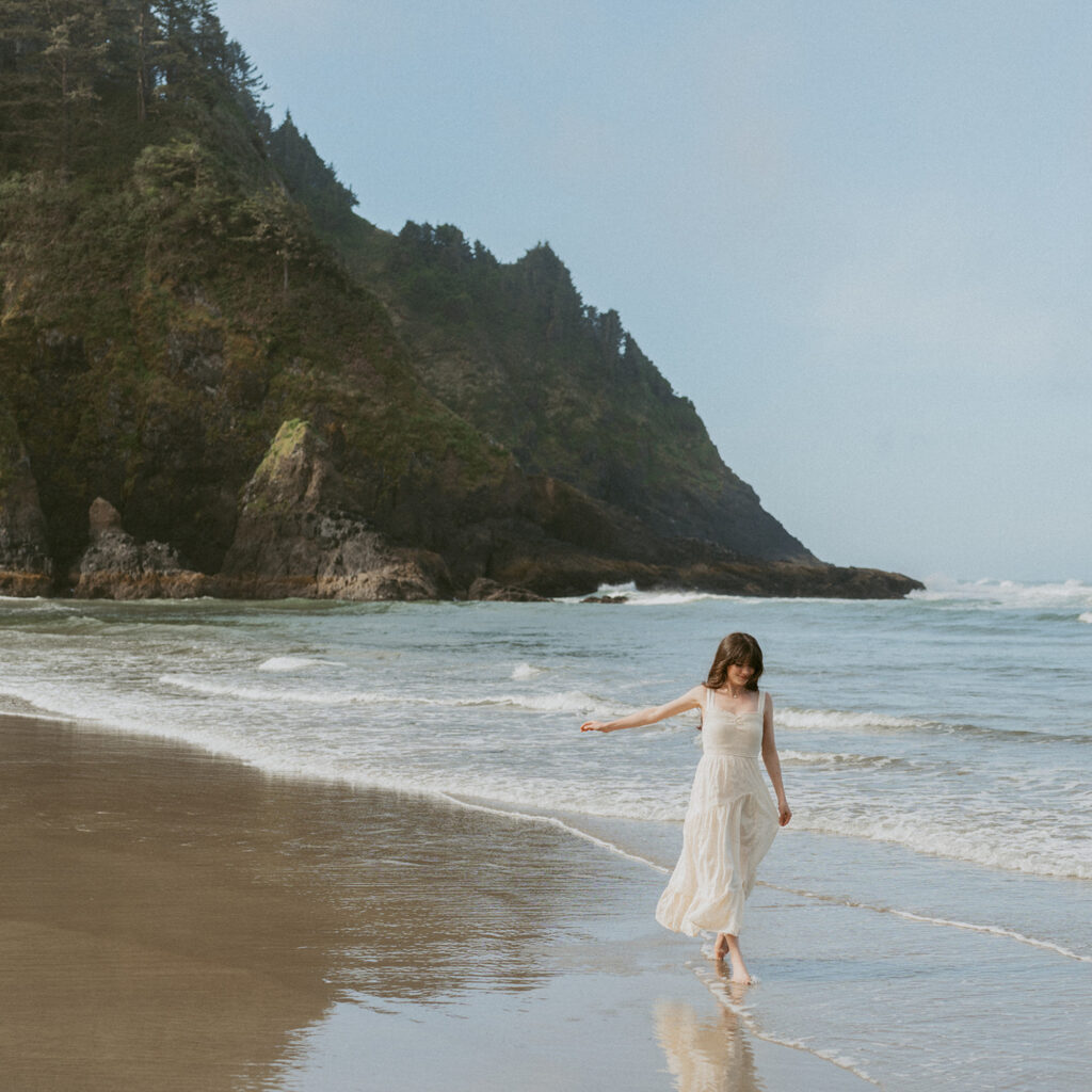 Woman in a white dress runs playfully through shallow surf on a beach in Florence, Oregon