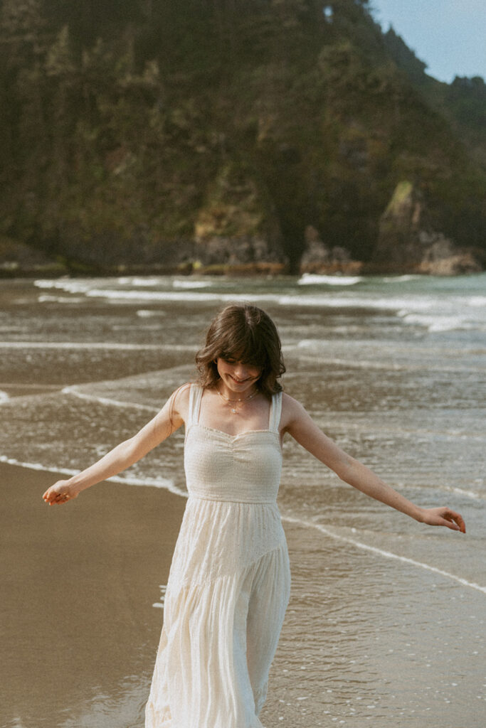 Woman in a white dress walking along a beach with gentle waves touching the shore