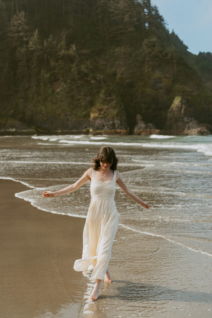 Woman in a white dress walking along a beach with gentle waves touching the shore