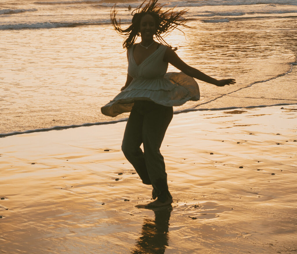 Woman dances joyfully on a beach as the sun sets