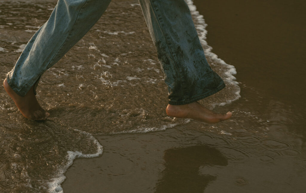 Woman walking barefoot along the shoreline with waves gently lapping at their feet