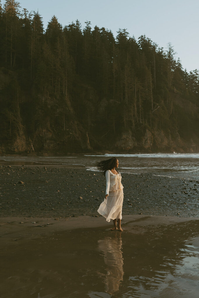 Woman in a flowing white dress standing on a tranquil beach, gazing towards the horizon
