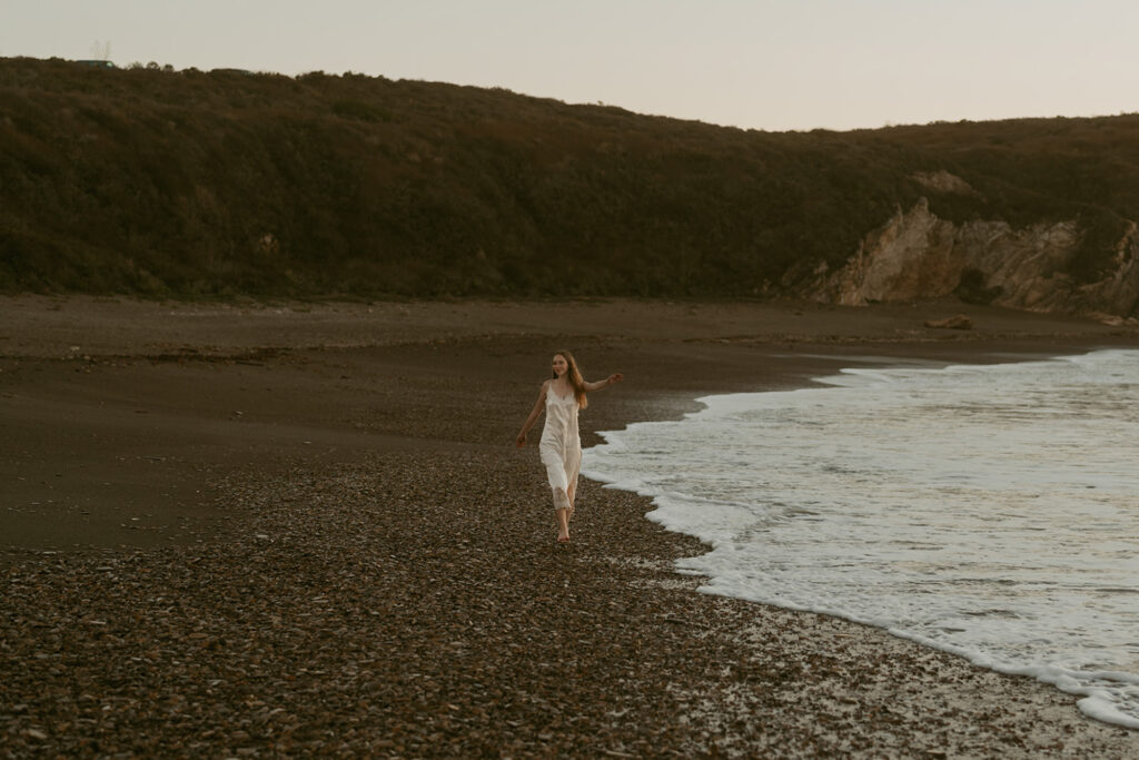 Woman in a white dress walks along a deserted, rocky beach