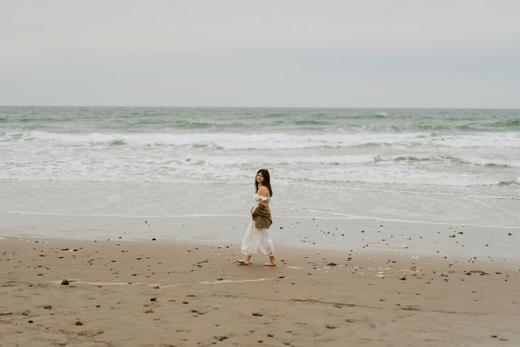 Woman running playfully on a sandy beach with the surf in the background for her senior session