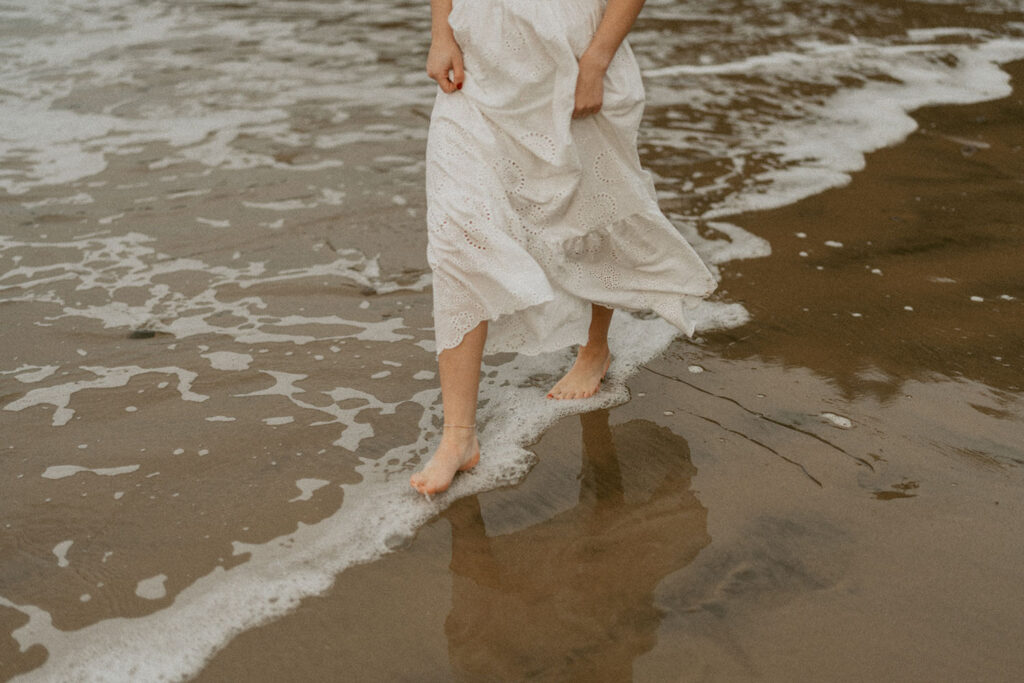 Close-up of woman's feet walking along the water's edge on a beach