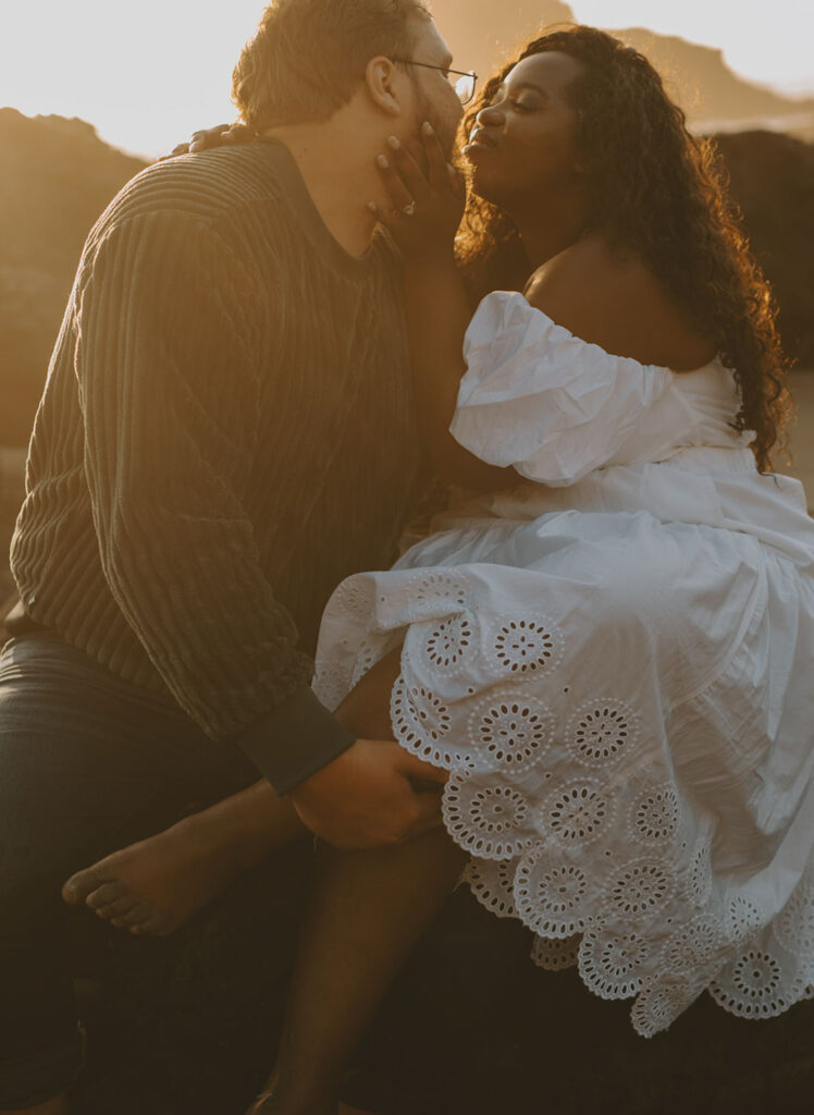 Engaged couple kissing on a beach rock at sunset in Oregon