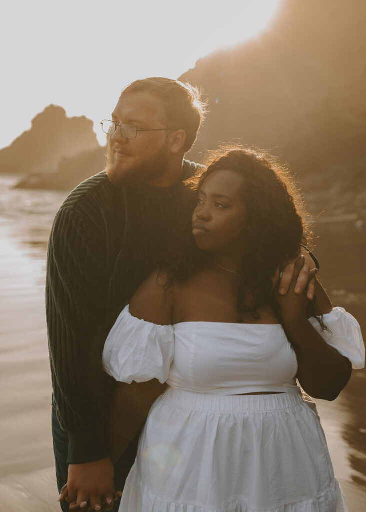 Engaged couple embracing at the beach with a sunset behind them