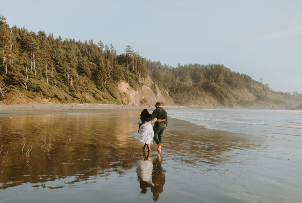 Engaged couple walking along the beach in Oregon, viewed from behind