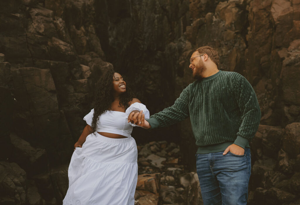 Engaged couple laughing and holding hands against a rocky backdrop in Oregon