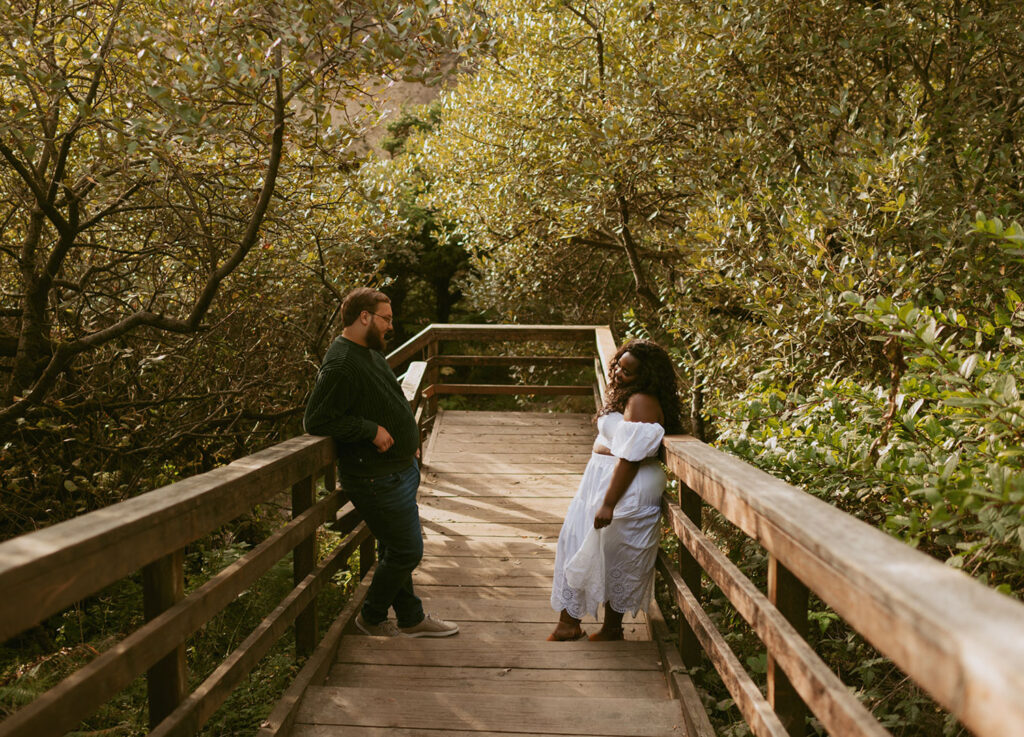 Engaged couple standing on a wooden bridge surrounded by lush foliage