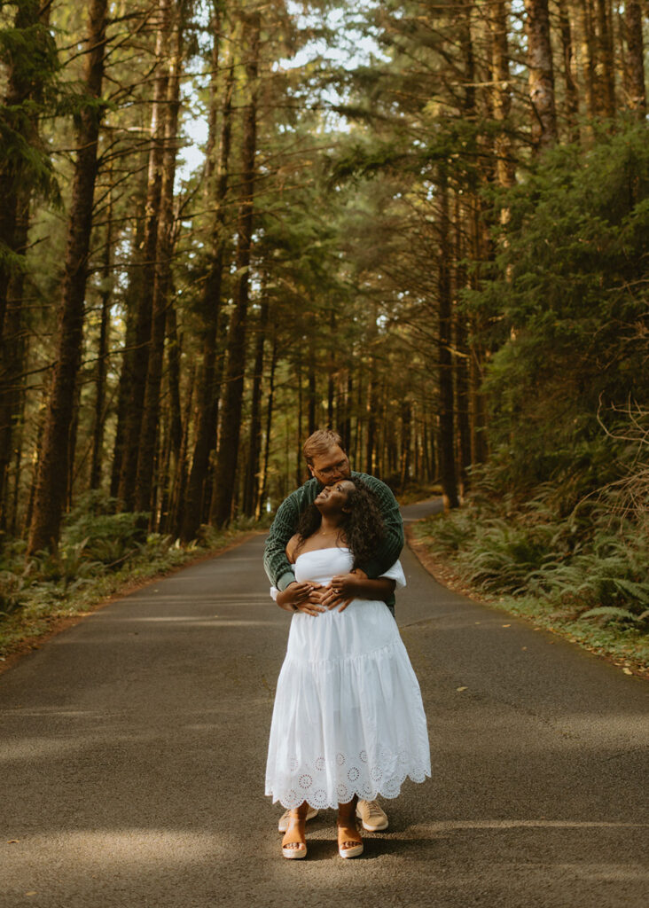 Couple embracing on a forest road surrounded by tall trees in Oregon for their Engagement Session