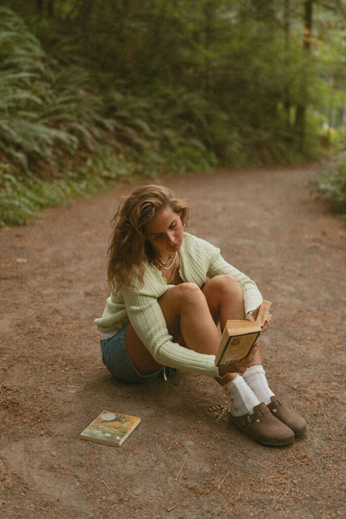 A senior reading a book on a forest trail for her senior session
