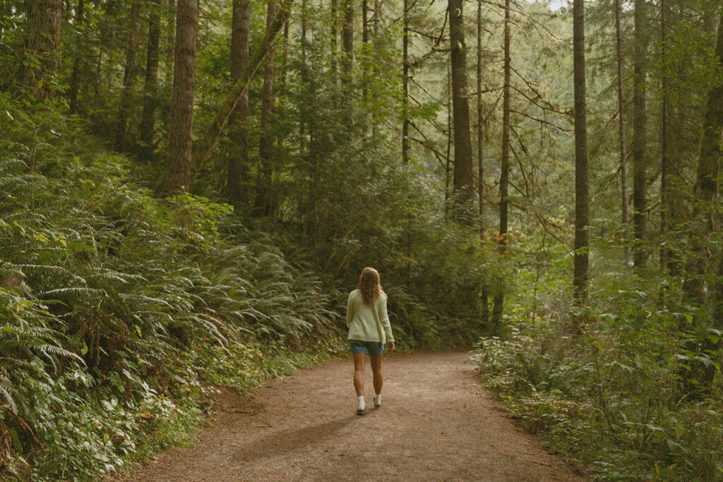 Woman walking away on a serene forest path surrounded by dense trees and ferns