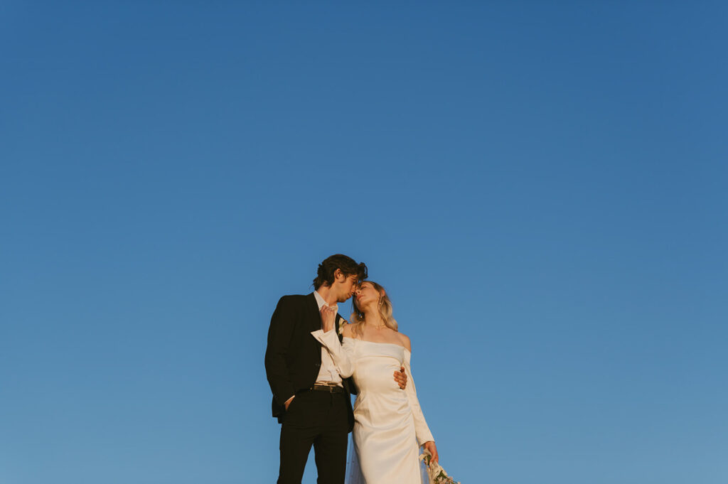 Couple sharing a kiss under a clear blue sky, embracing the simplicity of their elopement.
