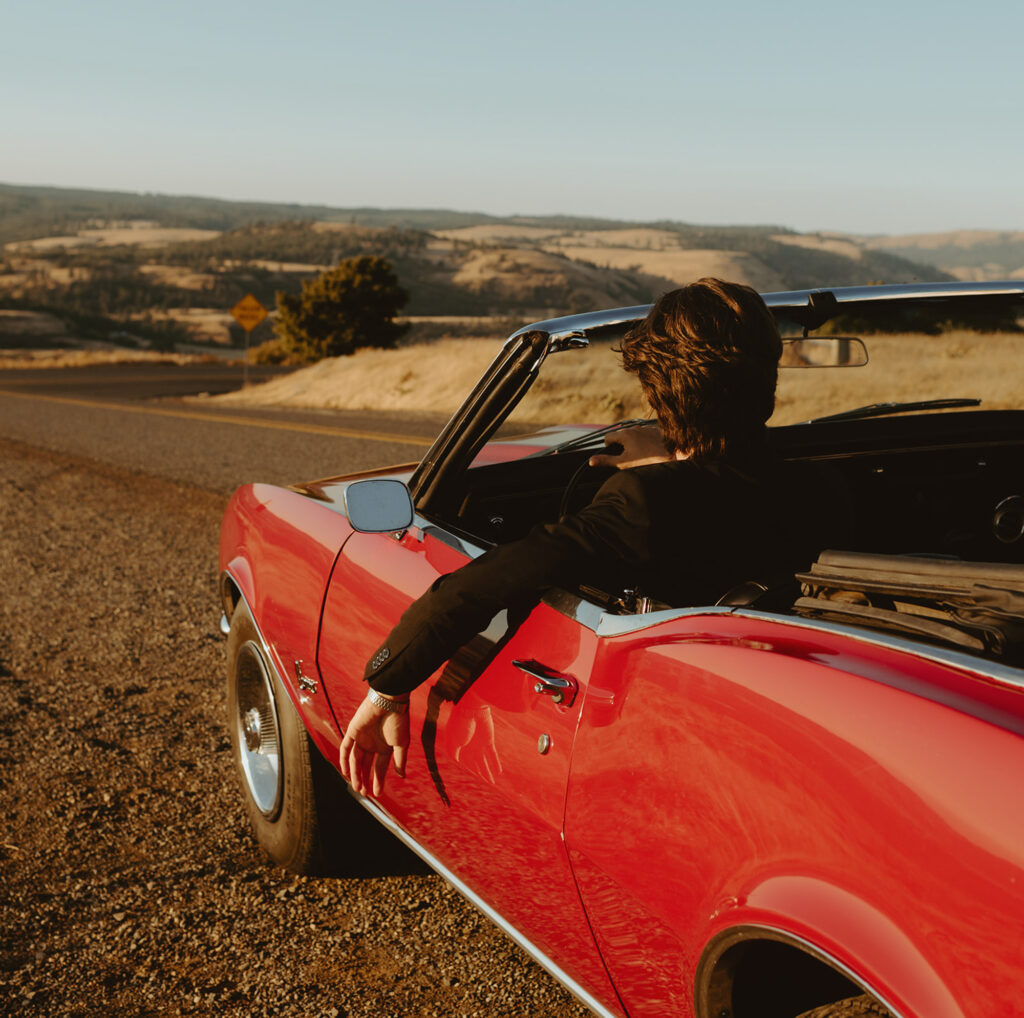 Groom relaxes in a red convertible, enjoying the scenic view after eloping