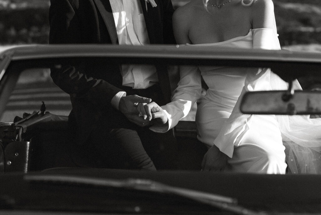 Newlyweds holding hands in the front seat of a classic car, celebrating their intimate elopement