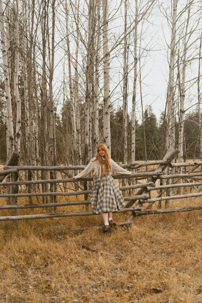 Senior girl standing on a wooden fence, arms outstretched, framed by aspen trees