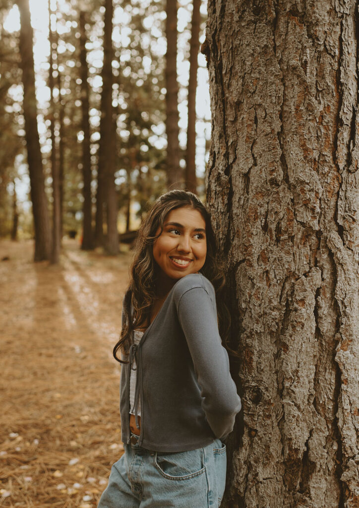 Smiling senior girl leaning against a tree for a photo session by a senior photographer in Bend