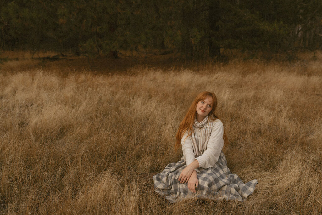 Senior girl sitting in a field, softly smiling with autumn tones around her