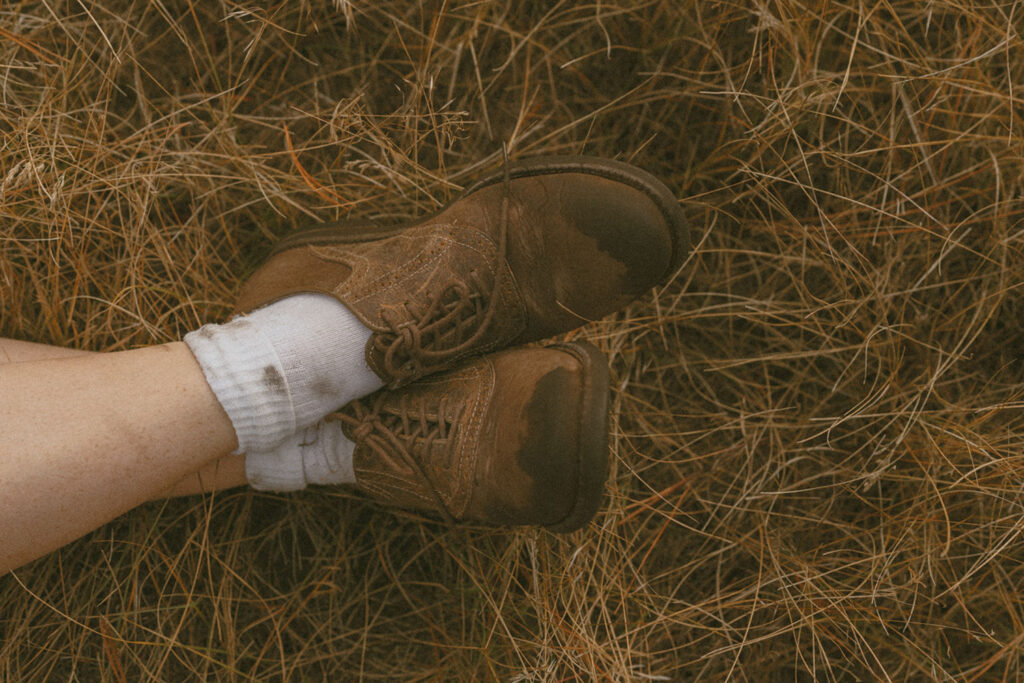 Close-up of worn brown boots resting in dried grass