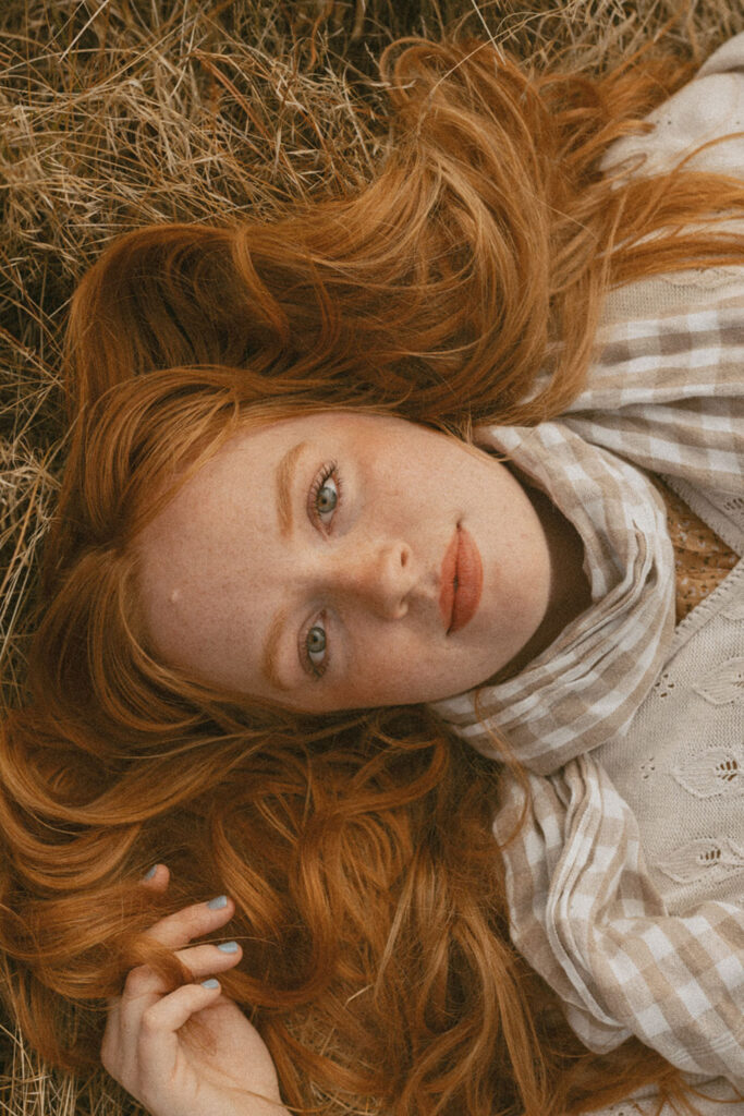 Close-up of senior girl lying in golden grass, gazing softly at the camera