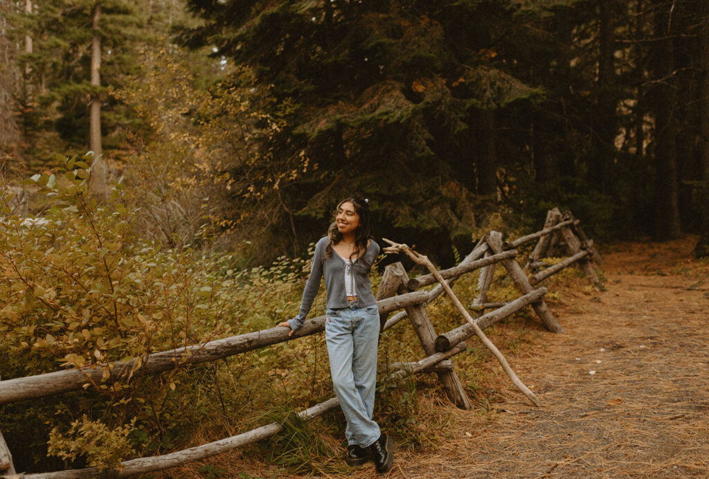 Senior girl in jeans and a cardigan, leaning on a wooden fence near Suttle Lake