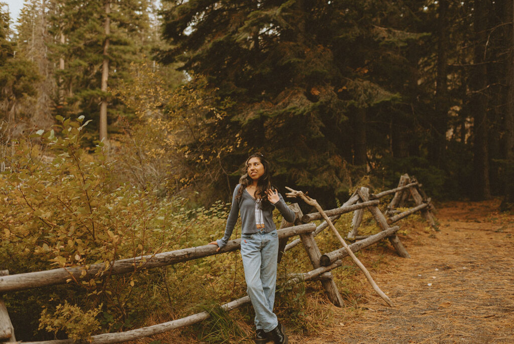 Senior girl in jeans and a cardigan, leaning on a wooden fence near Suttle Lake