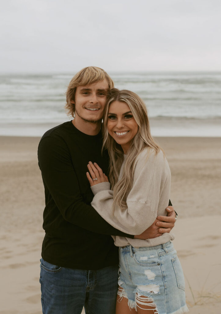 Callie and Nolan happily holding each other for their beach engagement photos