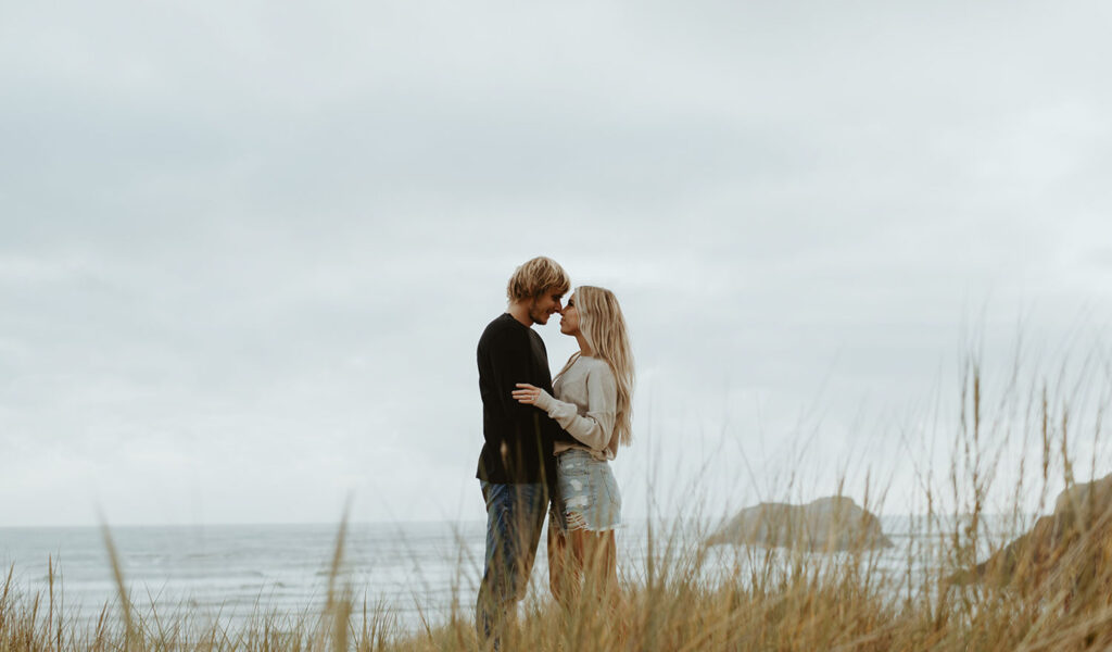 Callie and Nolan in a grassy area near the ocean, embracing and looking into each other's eyes