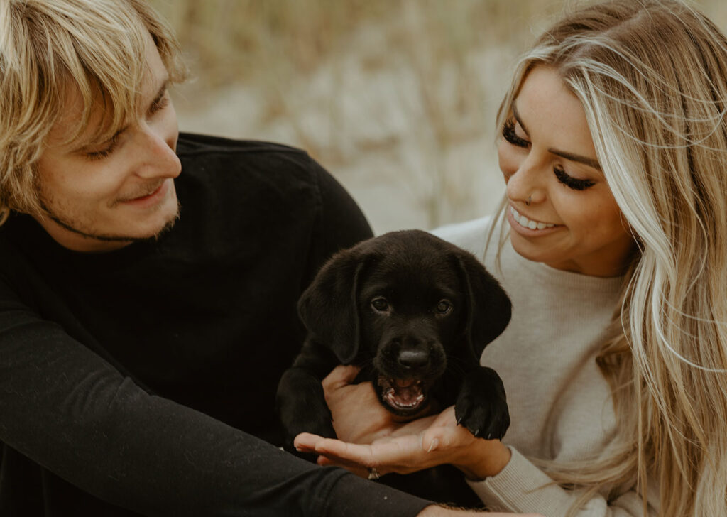 Callie and Nolan holding their little black lab puppy who's making a funny face