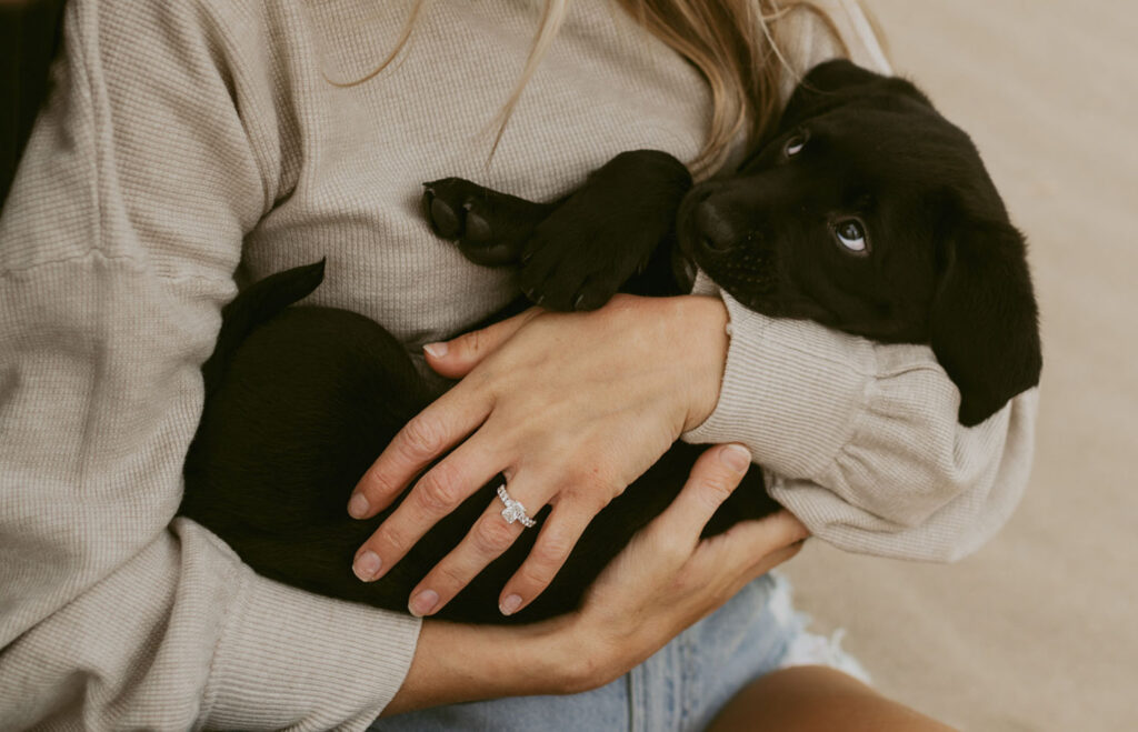 Callie cradles their black puppy in her arms, her engagement ring prominently displayed