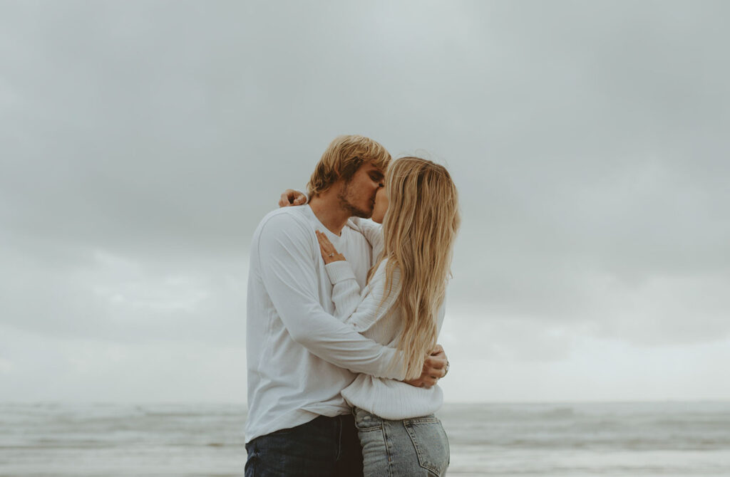 Callie and Nolan share a tender kiss on the beach, ocean waves in the background