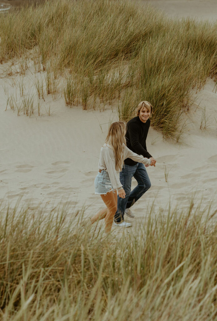 Callie and Nolan run hand in hand through the sand dunes, smiling.