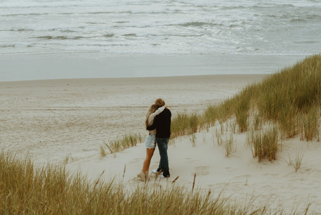 Callie and Nolan embraces on a sandy beach surrounded by tall grass