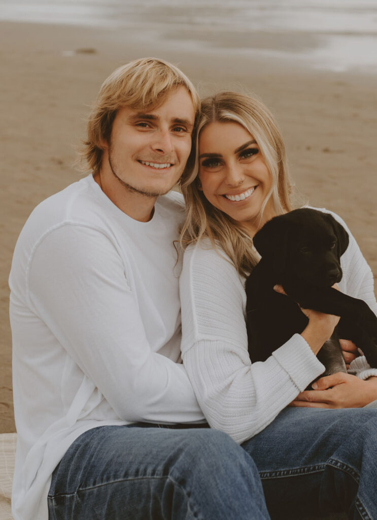 Callie and Nolan with their dog sitting on a beach smiling at the camera