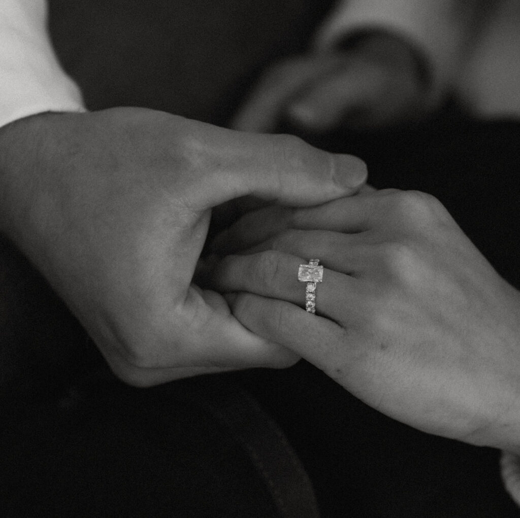 Black and white close-up of Nolan gently holding Callie’s hand, highlighting the engagement ring