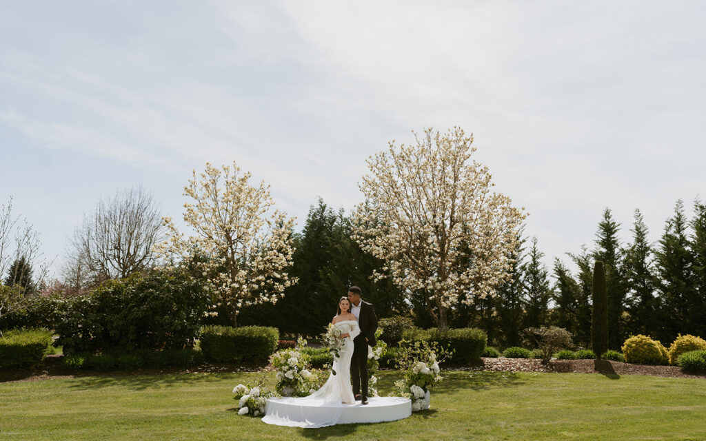 A bride and groom are standing on a white platform in a field.