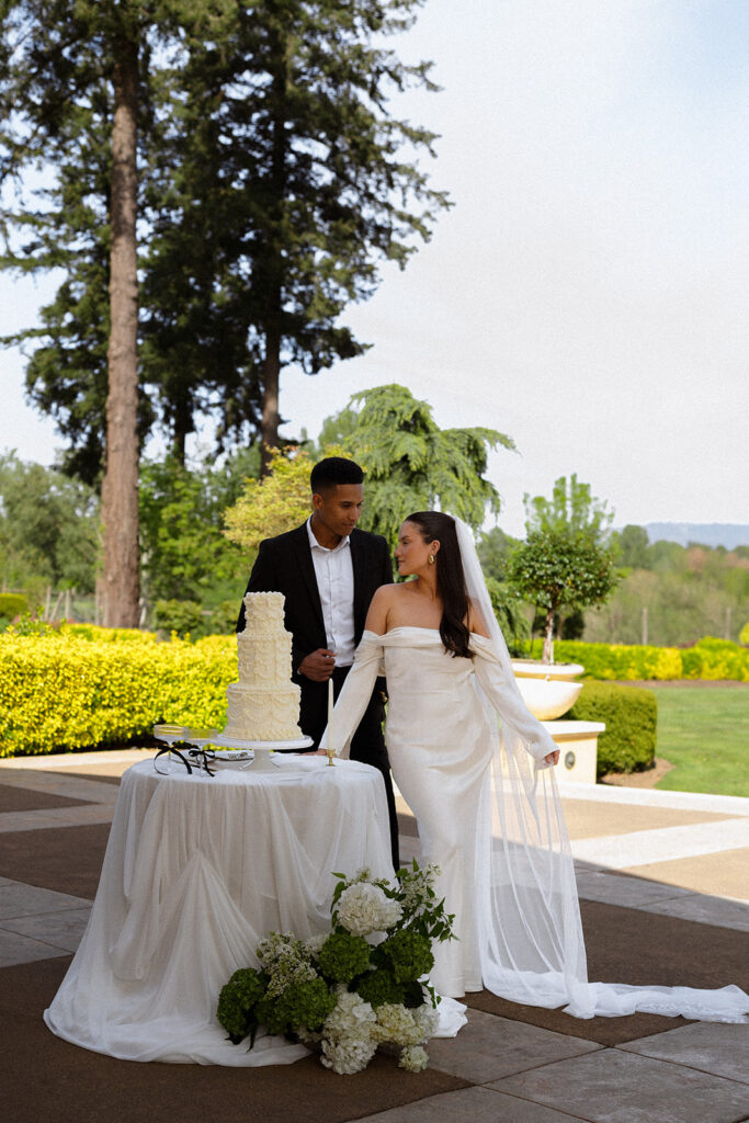 A bride and groom are standing in front of a cake table.